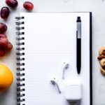 a notepad, pen, fruit, and a charger on a table