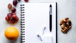 a notepad, pen, fruit, and a charger on a table
