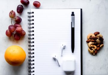 a notepad, pen, fruit, and a charger on a table