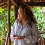 A smiling woman holding berries on a tropical porch.
