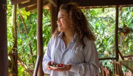 A smiling woman holding berries on a tropical porch.