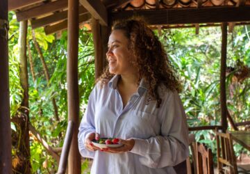 A smiling woman holding berries on a tropical porch.